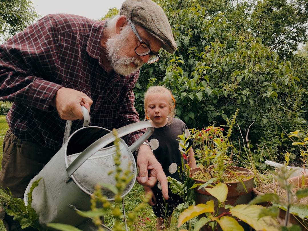 Older man enjoys teaching his grandaughter how to water the plants in the backyard